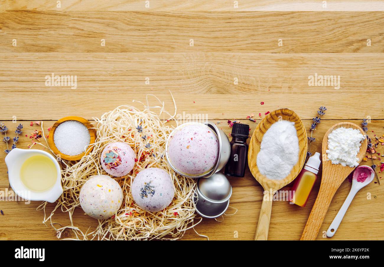 Making fizzy bath bombs at home concept. All the ingredients on table on wood spoons: cornstarch, essential oil, dye, citric acid, baking soda. Stock Photo