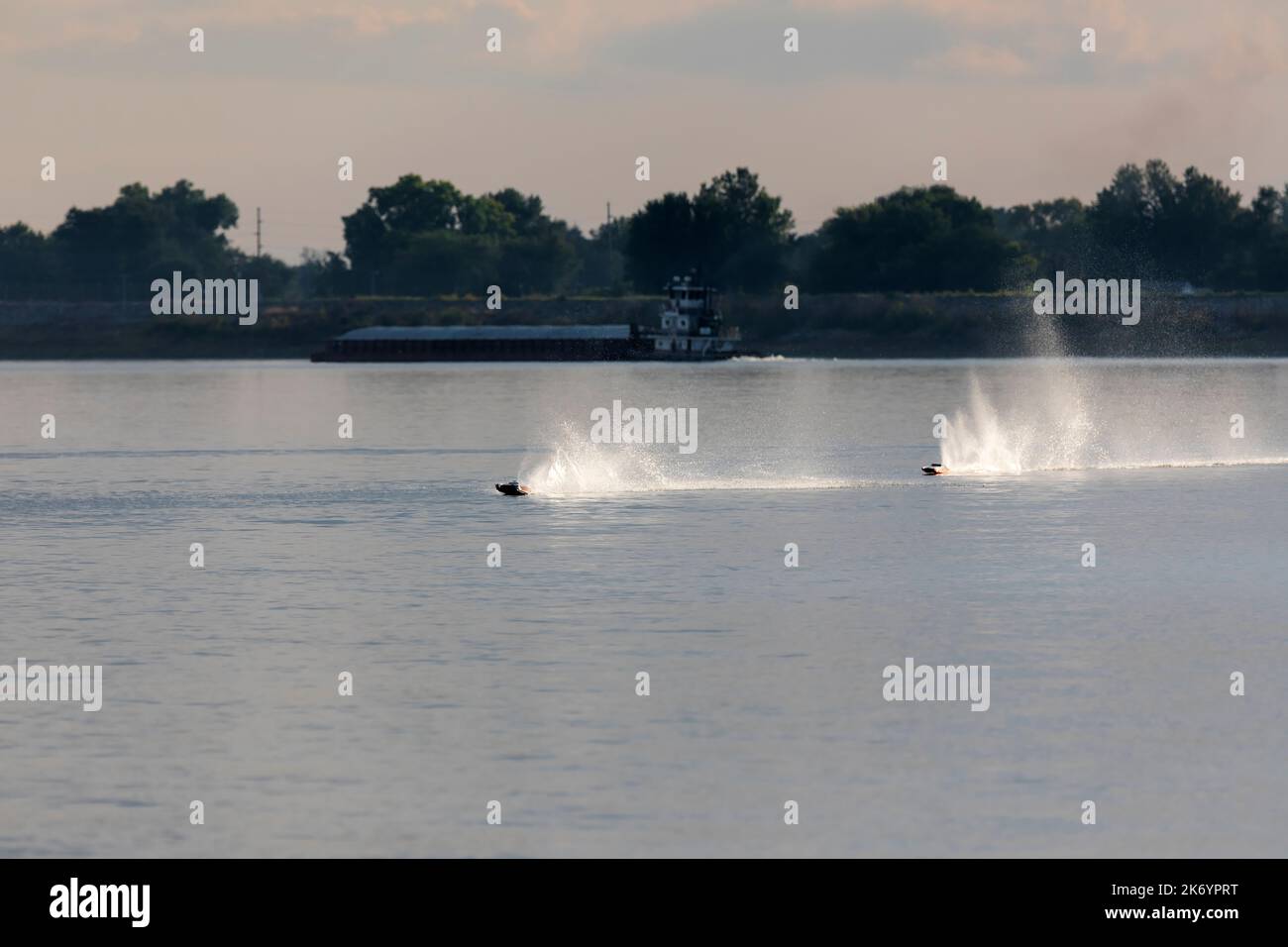 Racing high speed remote controlled boats on the Mississippi River near Muscatine, Iowa.  In the background a tow pushes a loaded barge down the river Stock Photo