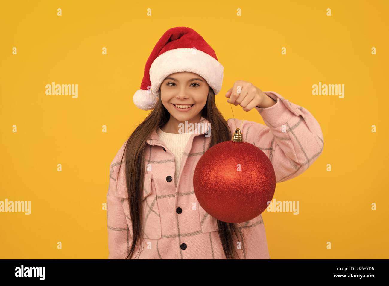 happy teen girl in santa claus hat hold christmas decorative ball on yellow background, new year Stock Photo