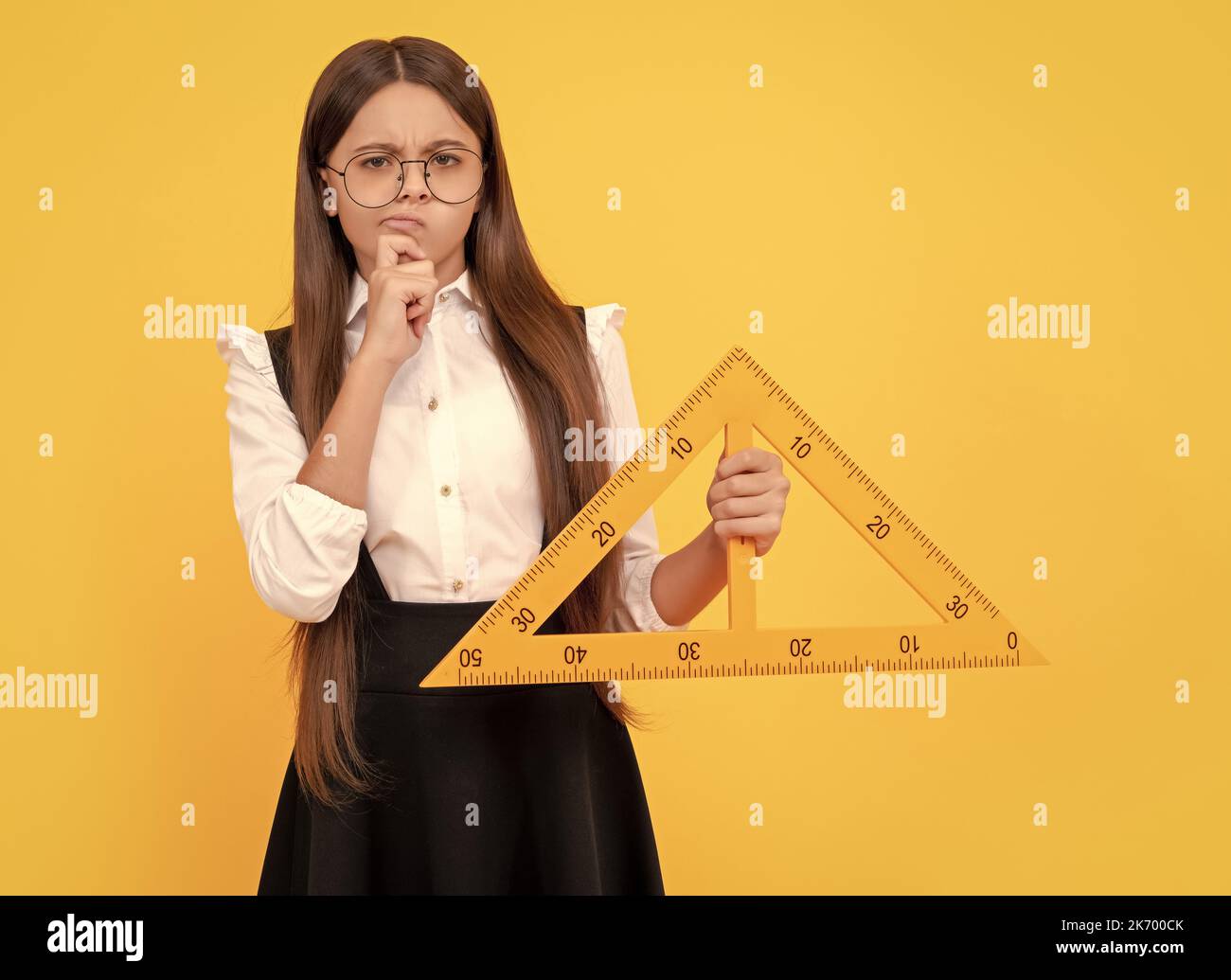 thinking teen girl in uniform and glasses hold mathematics triangle for measuring, measurement. Stock Photo