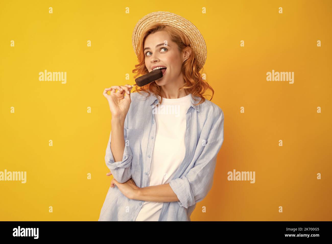 Young woman eat ice creams with chocolate glaze on yellow background