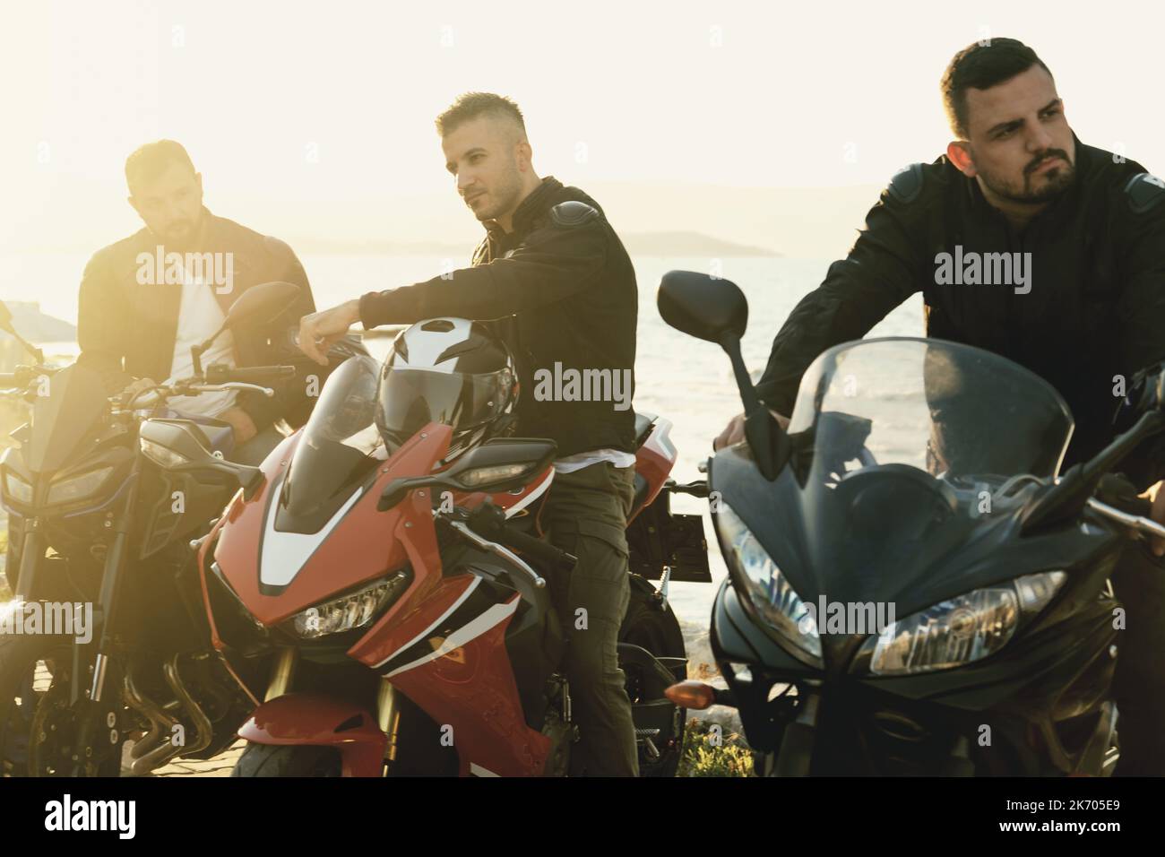 Three motorcyclye riders posing near the sea with their vehicles. Stock Photo