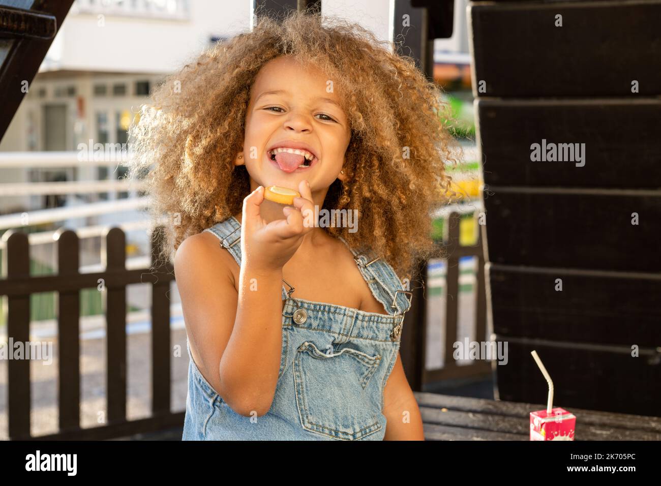 Cute kid girl eating sweet cakes outdoor in the park on sunny warm day Stock Photo