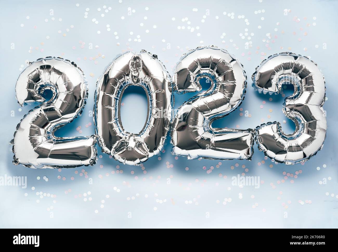 Shiny silber air balloon numbers on light blue background with confetti and decorations. 2023 New Year concept celebration Stock Photo