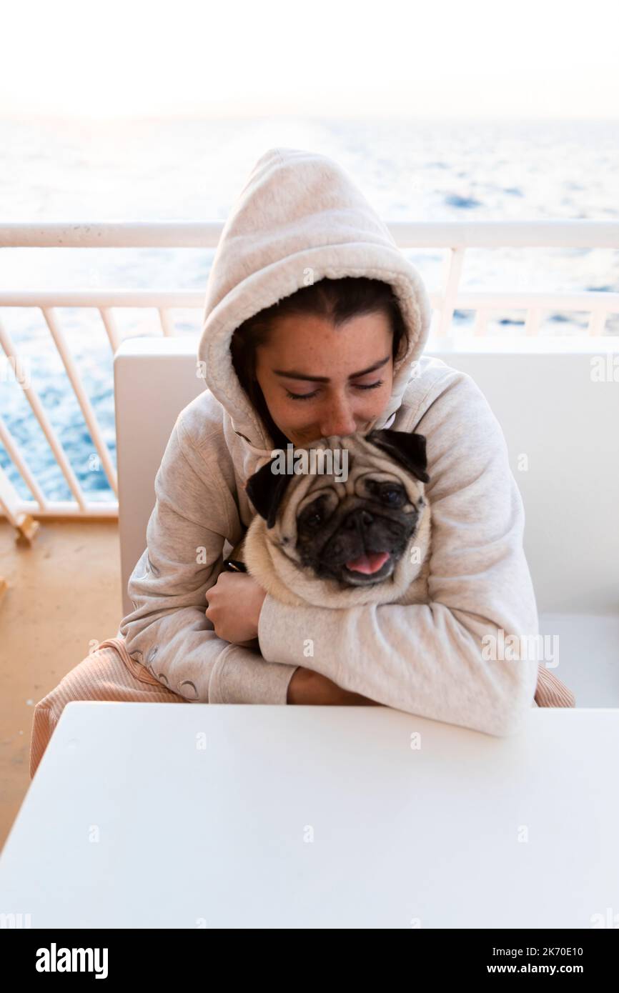 Woman in hoodie with pug on ferry boat Stock Photo