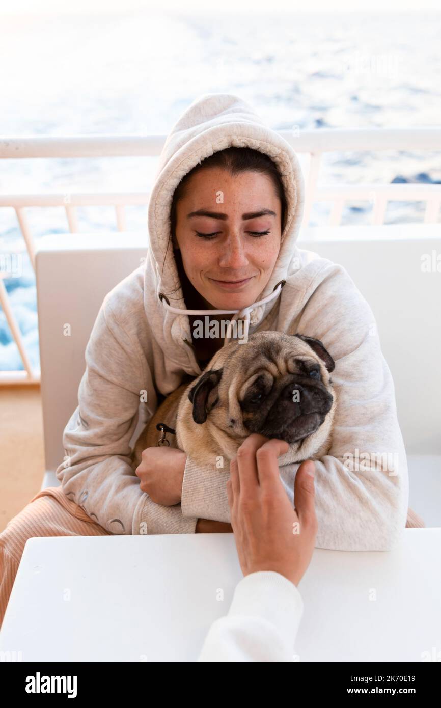 Woman in hoodie with pug on ferry boat Stock Photo
