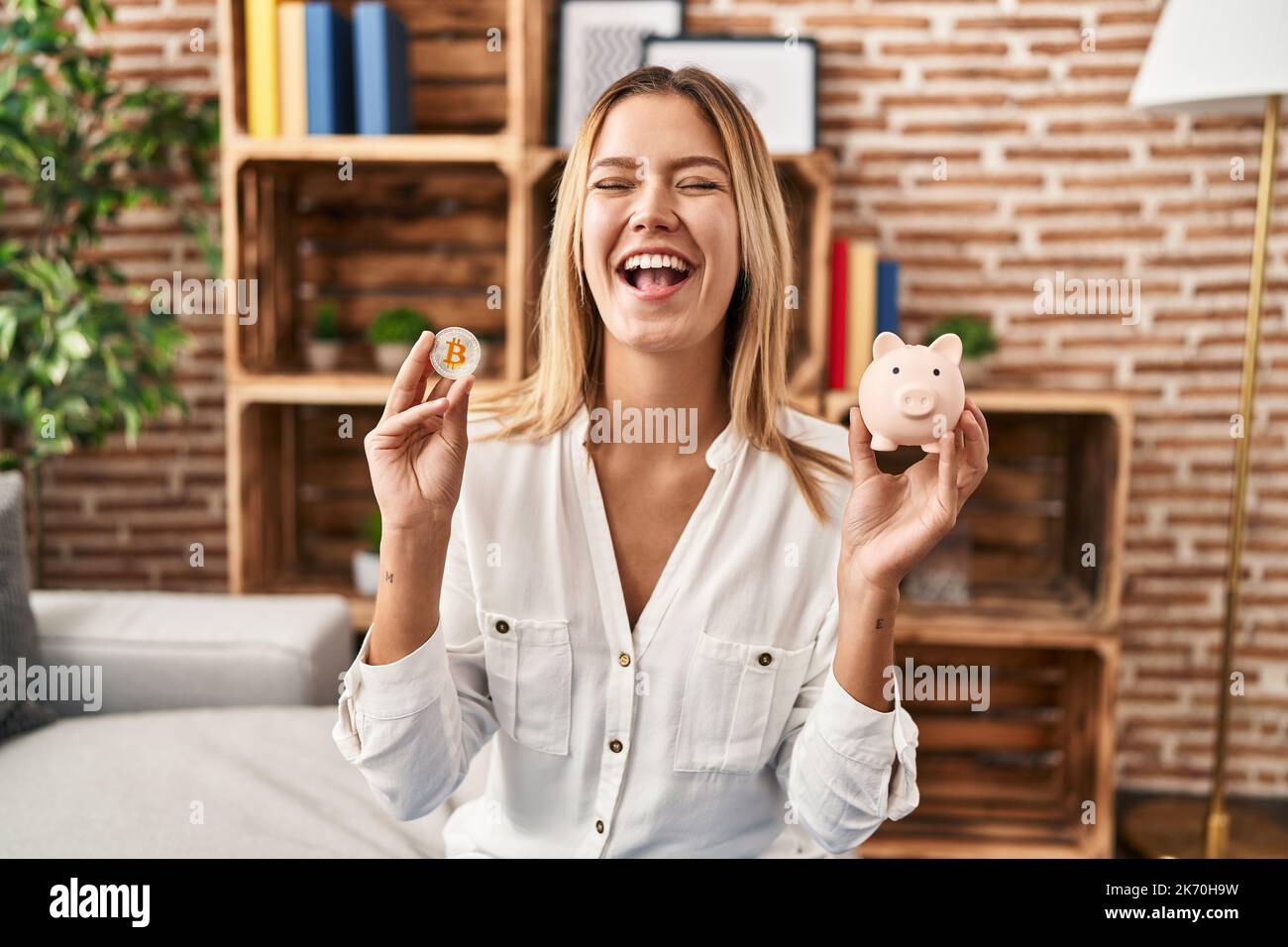 Young blonde woman holding piggy bank and bitcoin smiling and laughing hard  out loud because funny crazy joke Stock Photo - Alamy