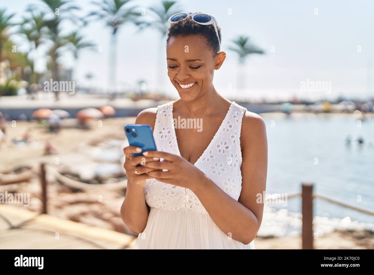 African american woman smiling confident using smartphone at seaside ...