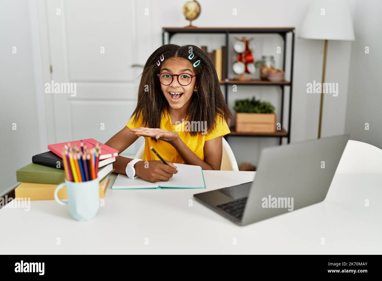 Young african american girl doing homework at home pointing aside with ...