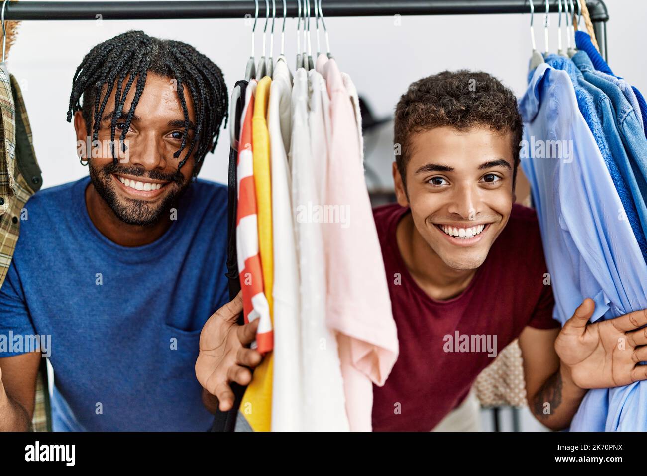 Two men friends smiling confident appearing through rack at clothing ...