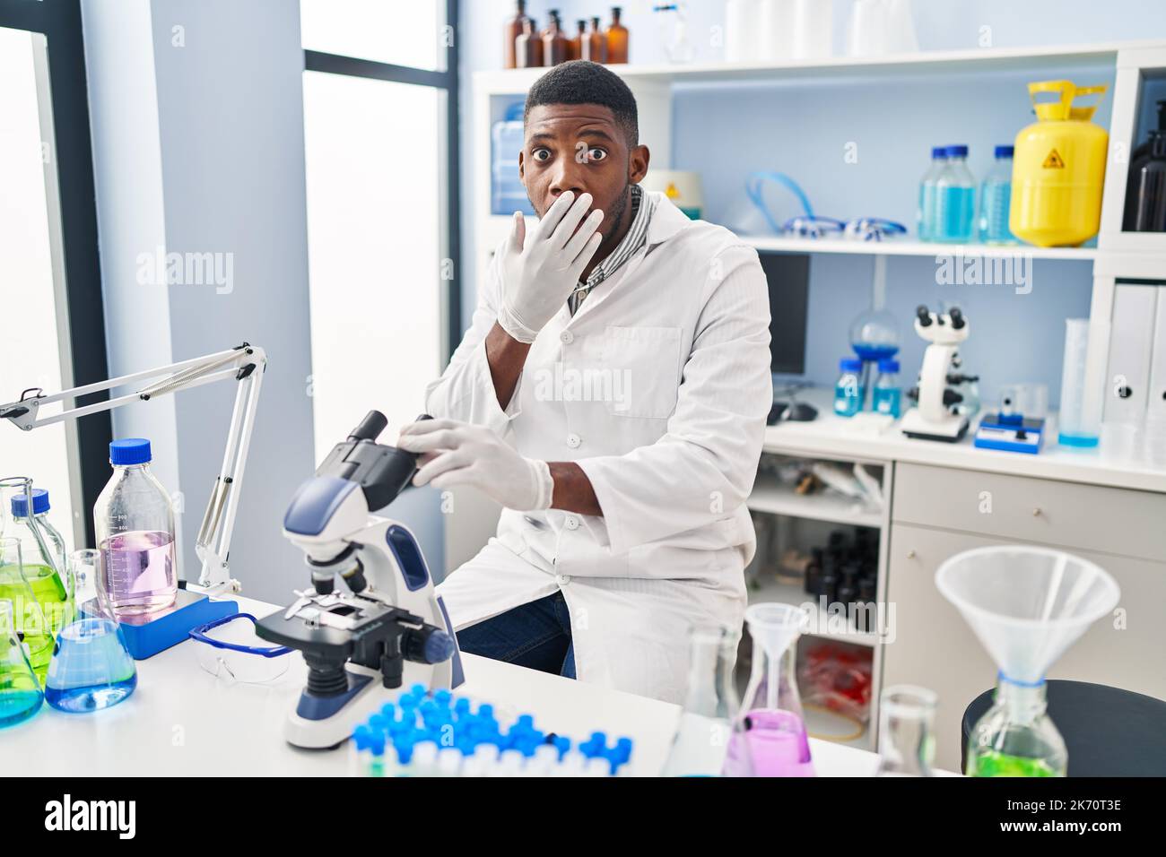African American Man Working At Scientist Laboratory Covering Mouth With Hand Shocked And 