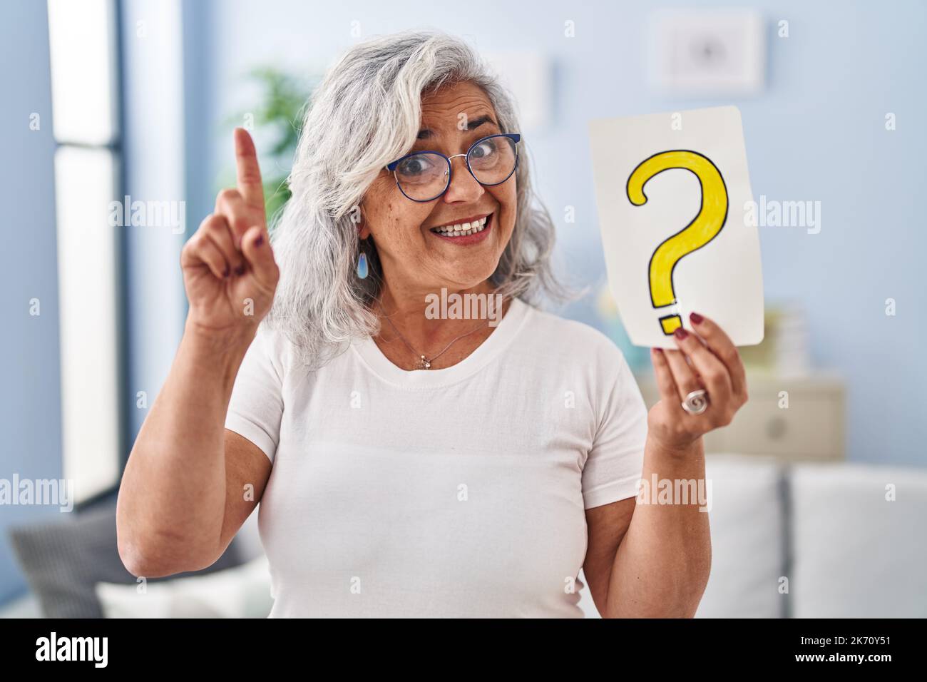 Middle age woman with grey hair holding question mark surprised with an ...