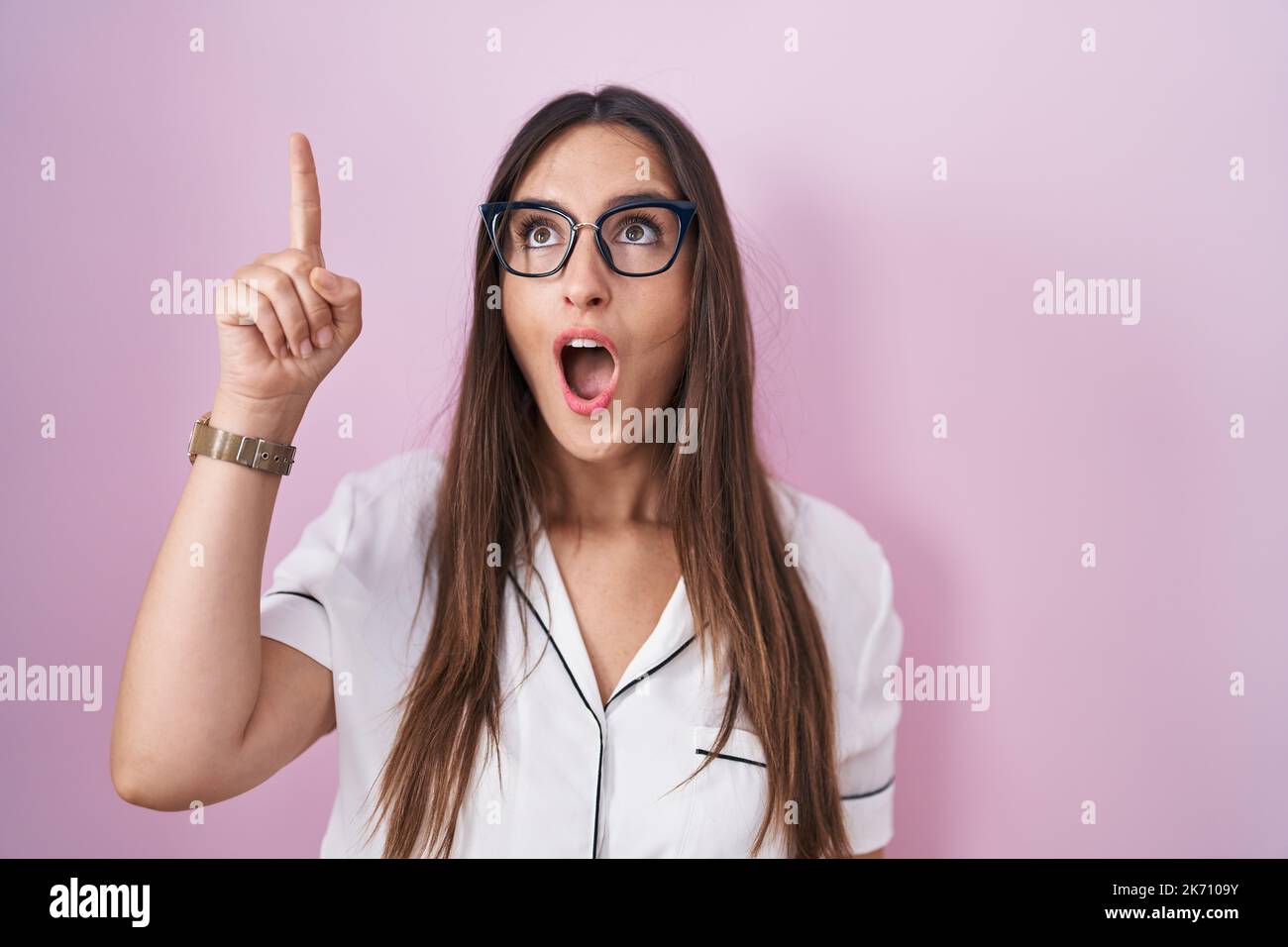 Young brunette woman wearing glasses standing over pink background ...