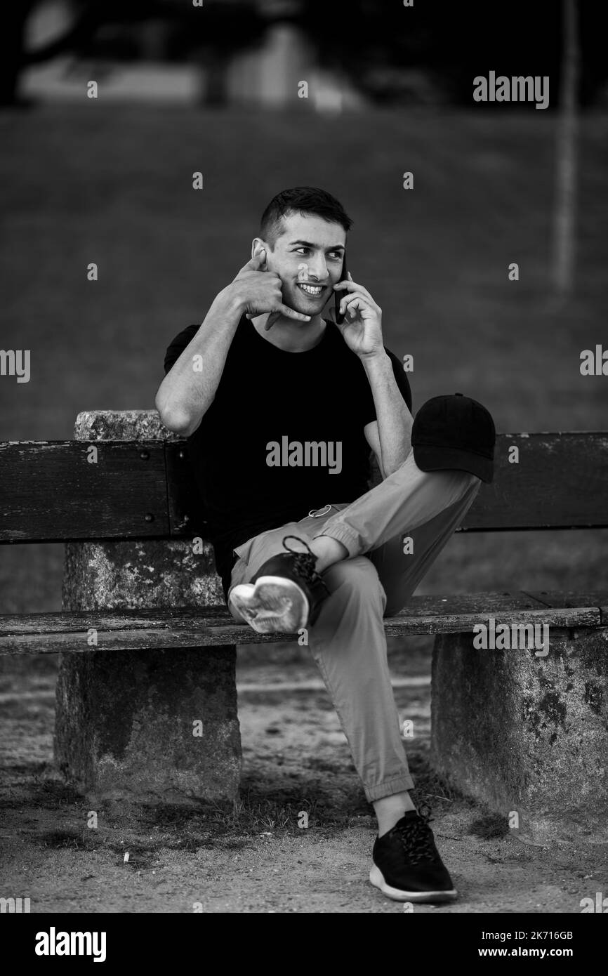 A handsome young man sitting on a bench talking on his cell phone. Black and white photo. Stock Photo