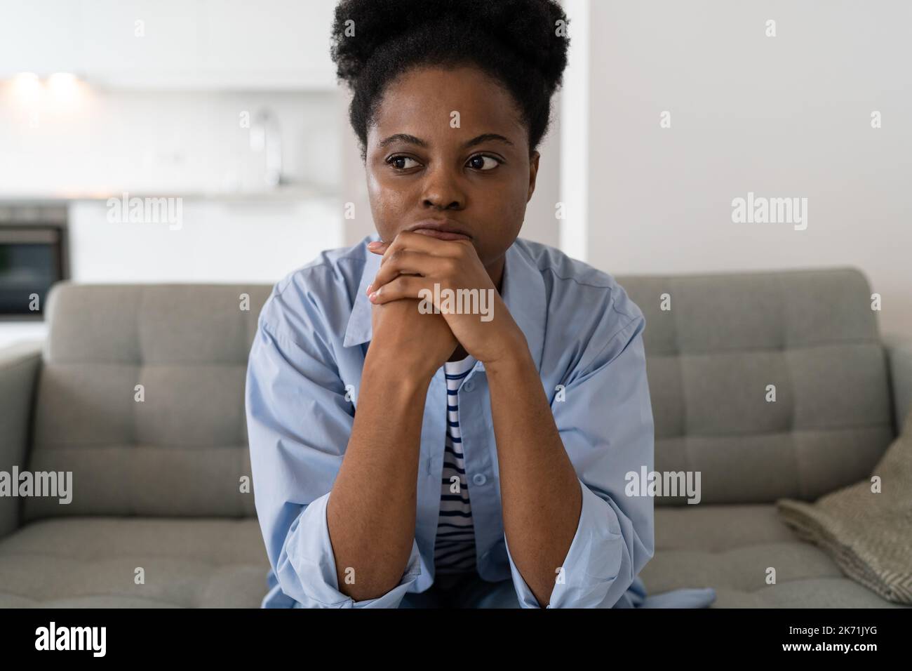 Tense young African American woman eflects on everyday problems related to crisis sits on sofa Stock Photo