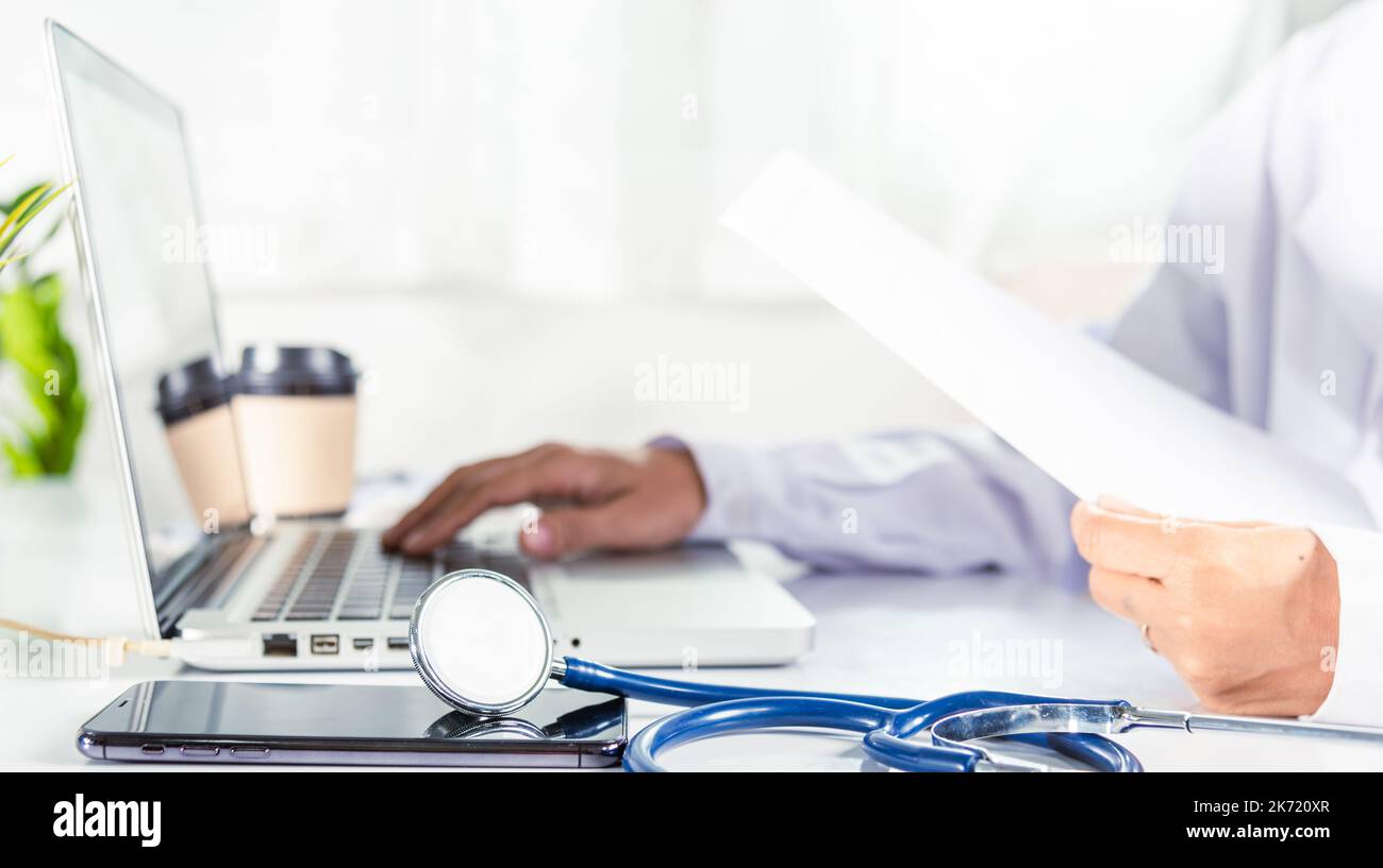 Closeup of doctor or nurse woman in uniform with stethoscope typing information of patient prescription from paperwork medical history form into lapto Stock Photo