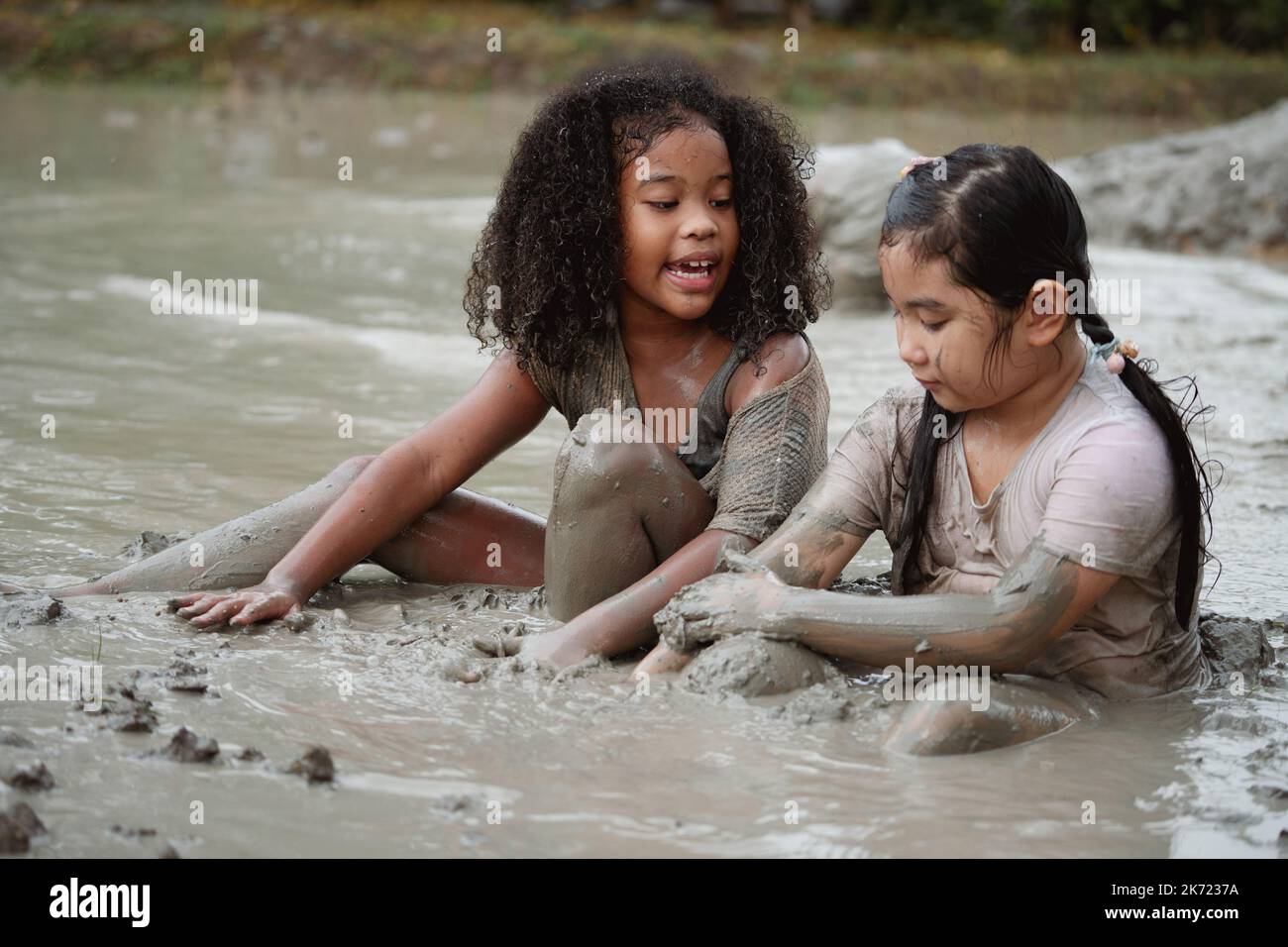 Group of happy children girl playing in wet mud puddle during raining in rainy season. Stock Photo