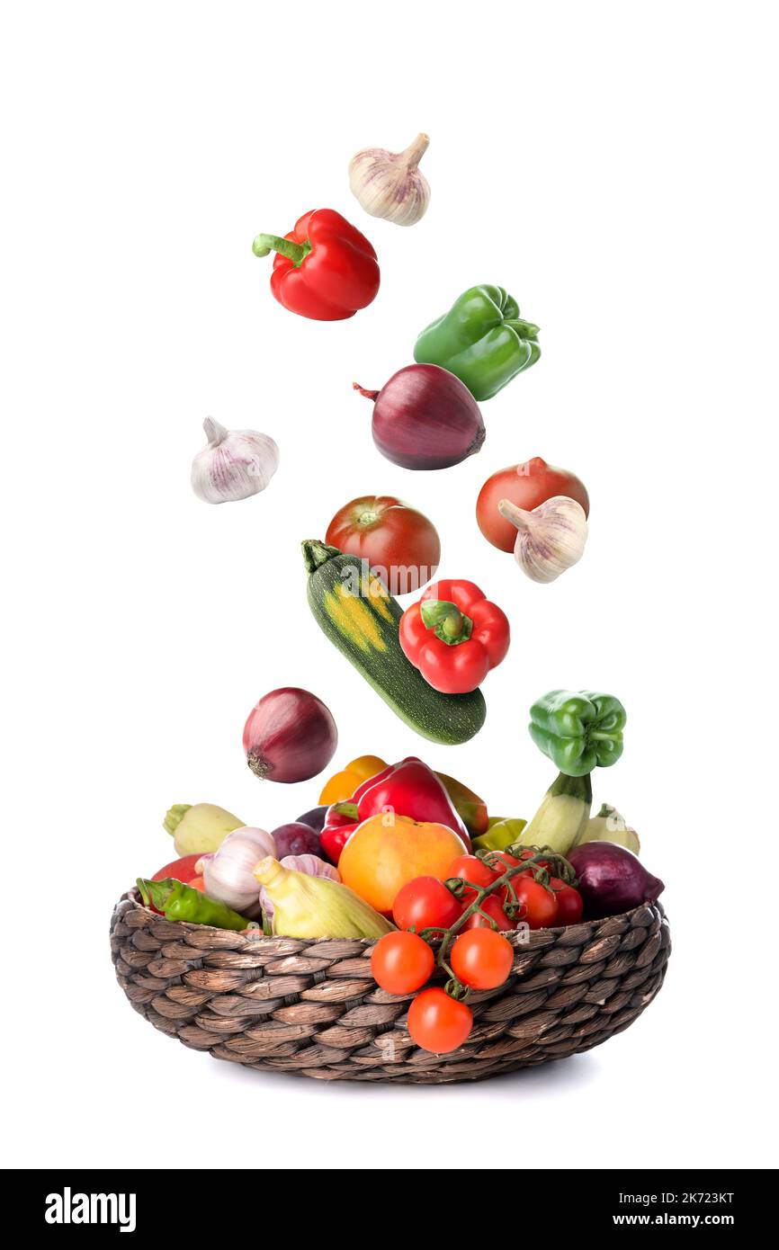 Many healthy vegetables falling into wicker basket on white background Stock Photo