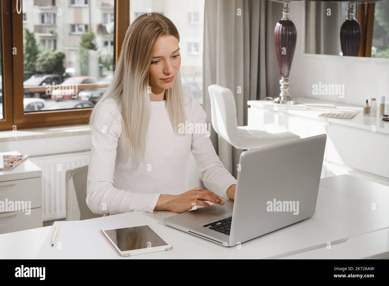 Woman works at the reception in a beauty salon. Typing something on laptop and talks on the phone with client, making appointments in studio Stock Photo