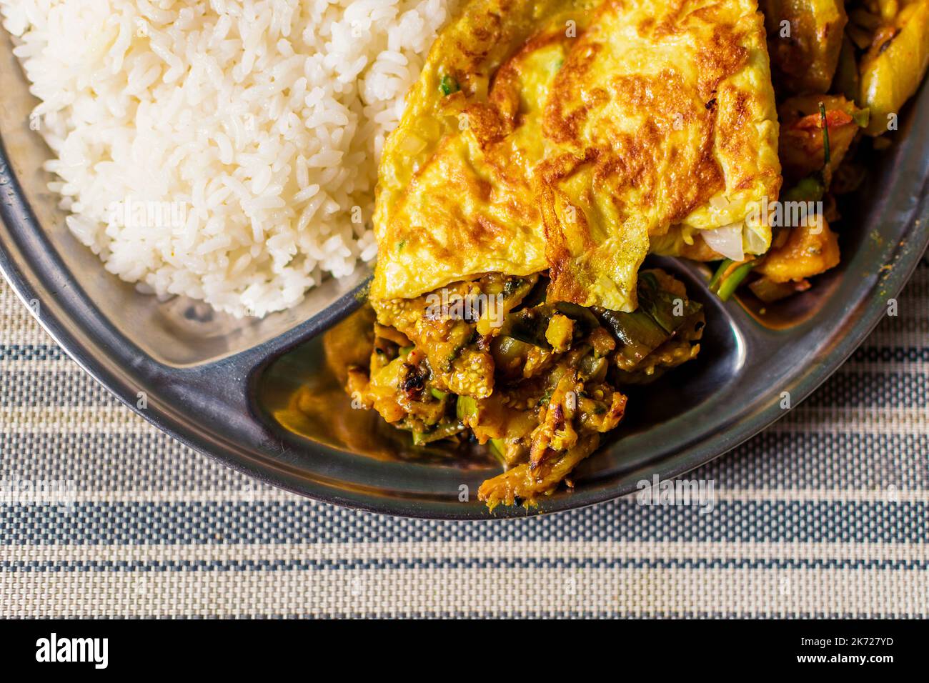 Steamed rice lentil dal mix vegetables Indian curry and an omelet on a lunch plate Bengali lunch