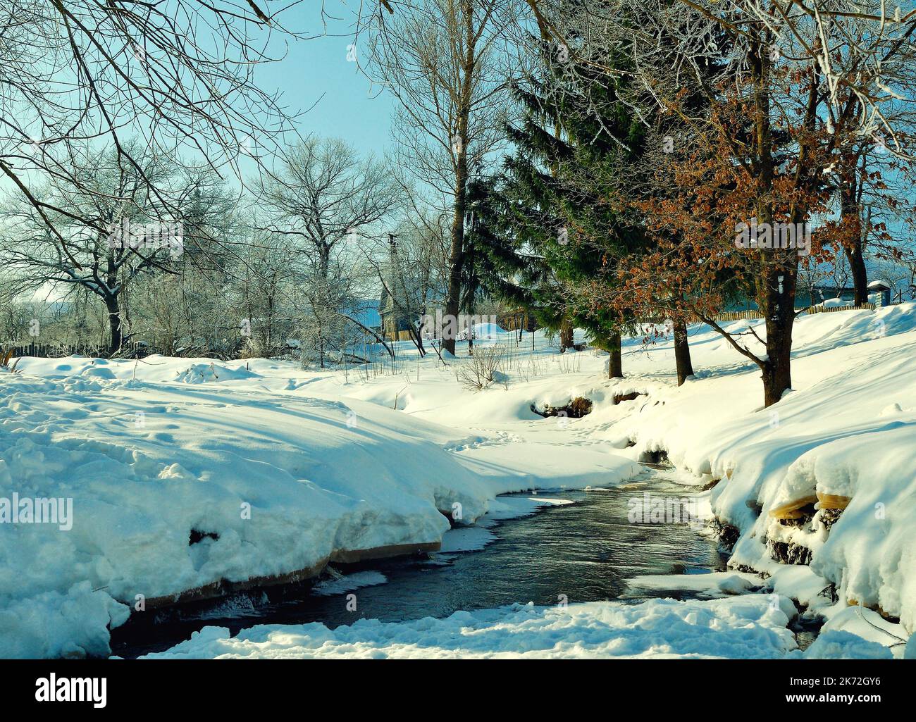 Winter landscape in sunny weather, winter view of rural houses near the river and winter snowdrifts on the foreground Stock Photo