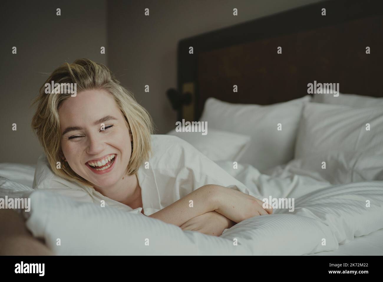 Blond woman laughing in bedroom Stock Photo