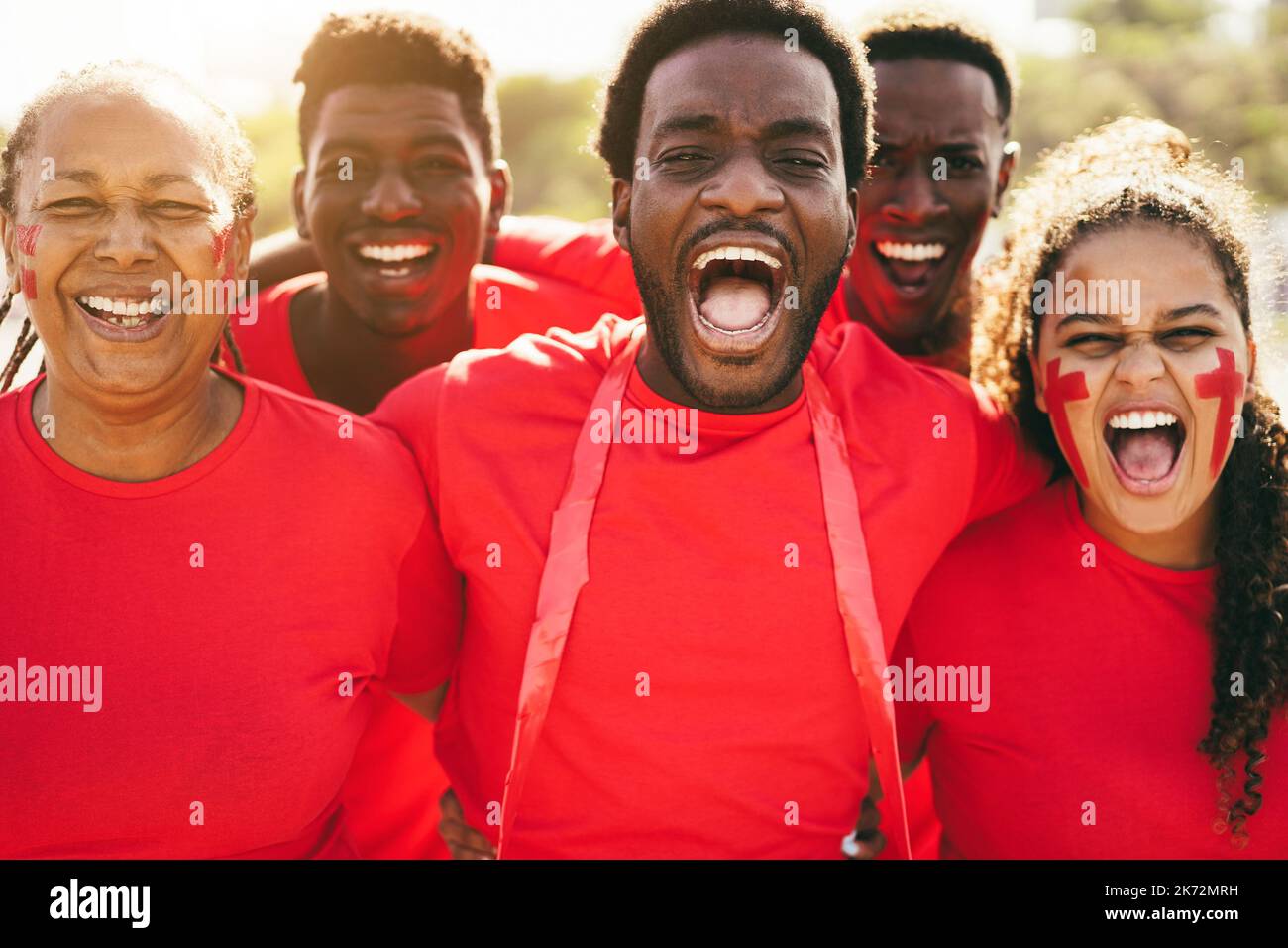 African red sport fans screaming while supporting their team - Football supporters having fun at competition event - Focus on center man face Stock Photo