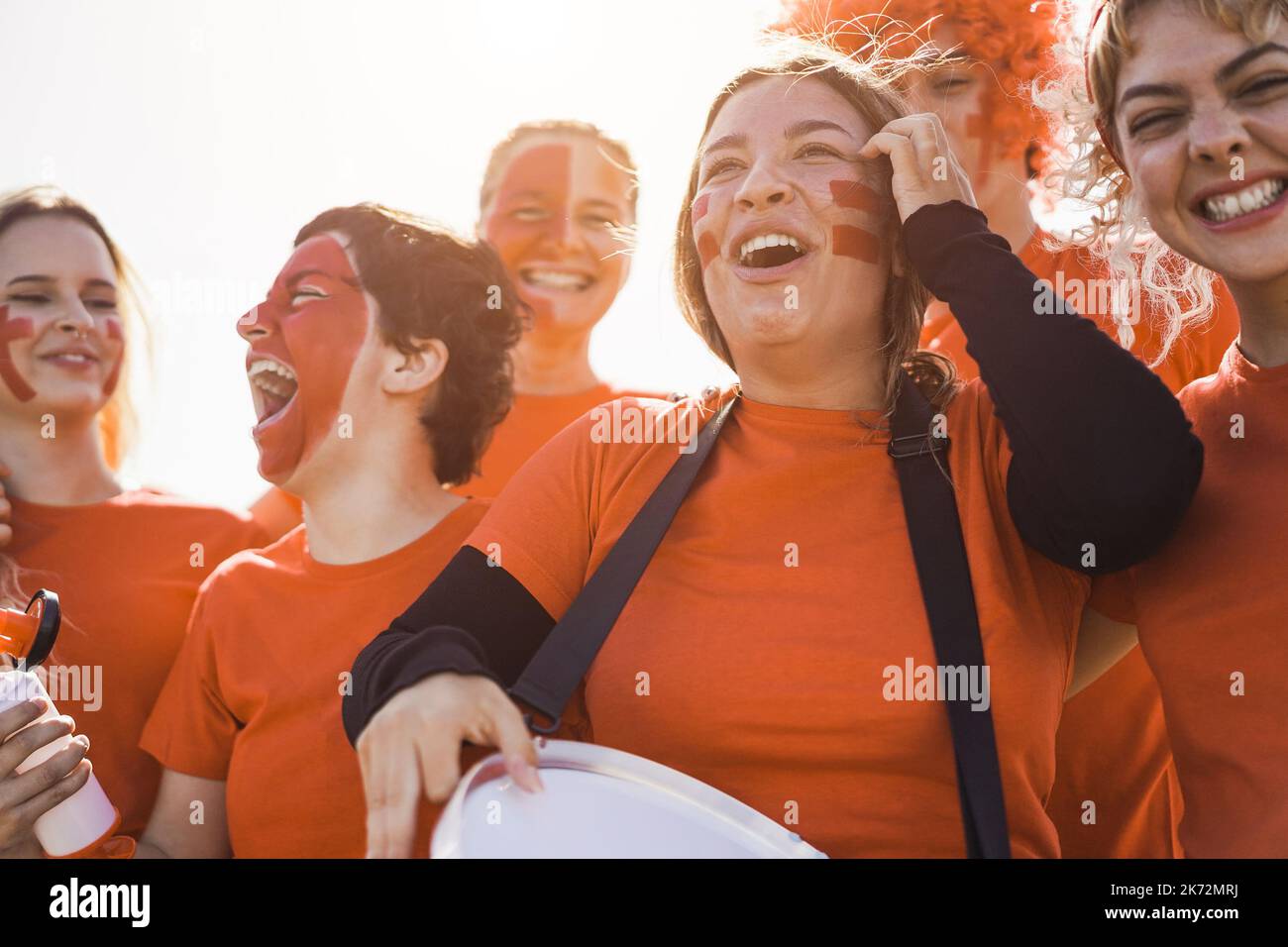 Orange sport football fans screaming while supporting their team out of the stadium - Focus on girl holding drum Stock Photo