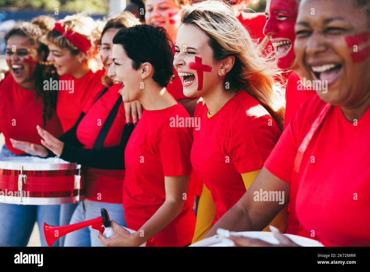 Multiracial red sport fans screaming while supporting their team - Football supporters having fun at competition event - Focus on center girl face Stock Photo