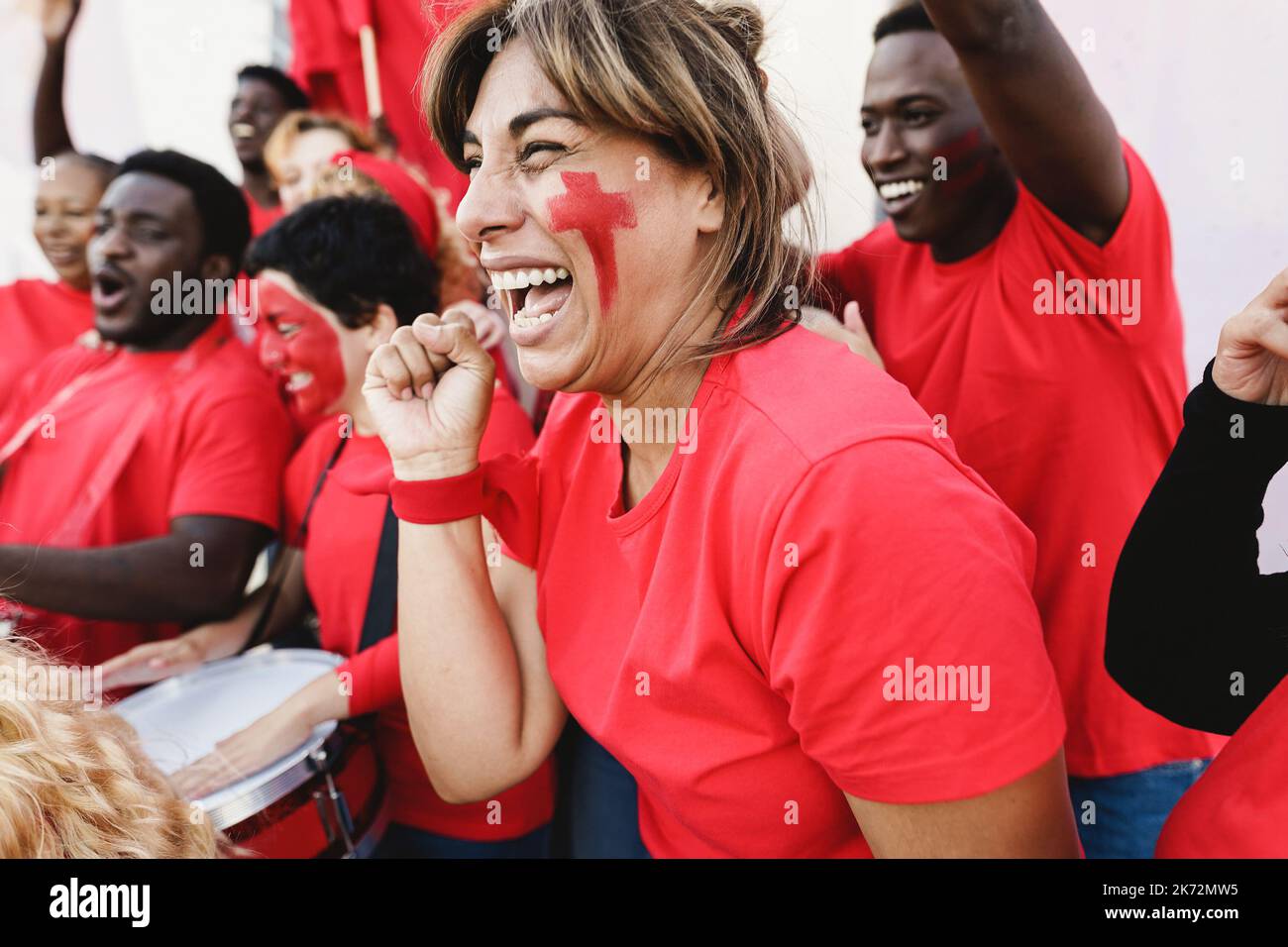Multiracial red sport fans screaming while supporting their team - Football supporters having fun at competition event - Soft focus on latin woman fac Stock Photo