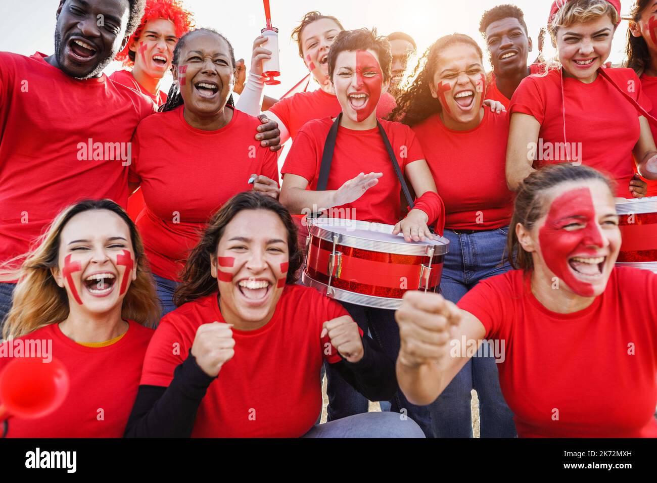 Multiracial red sport fans screaming while supporting their team - Football supporters having fun at competition event - Focus on center girl face Stock Photo