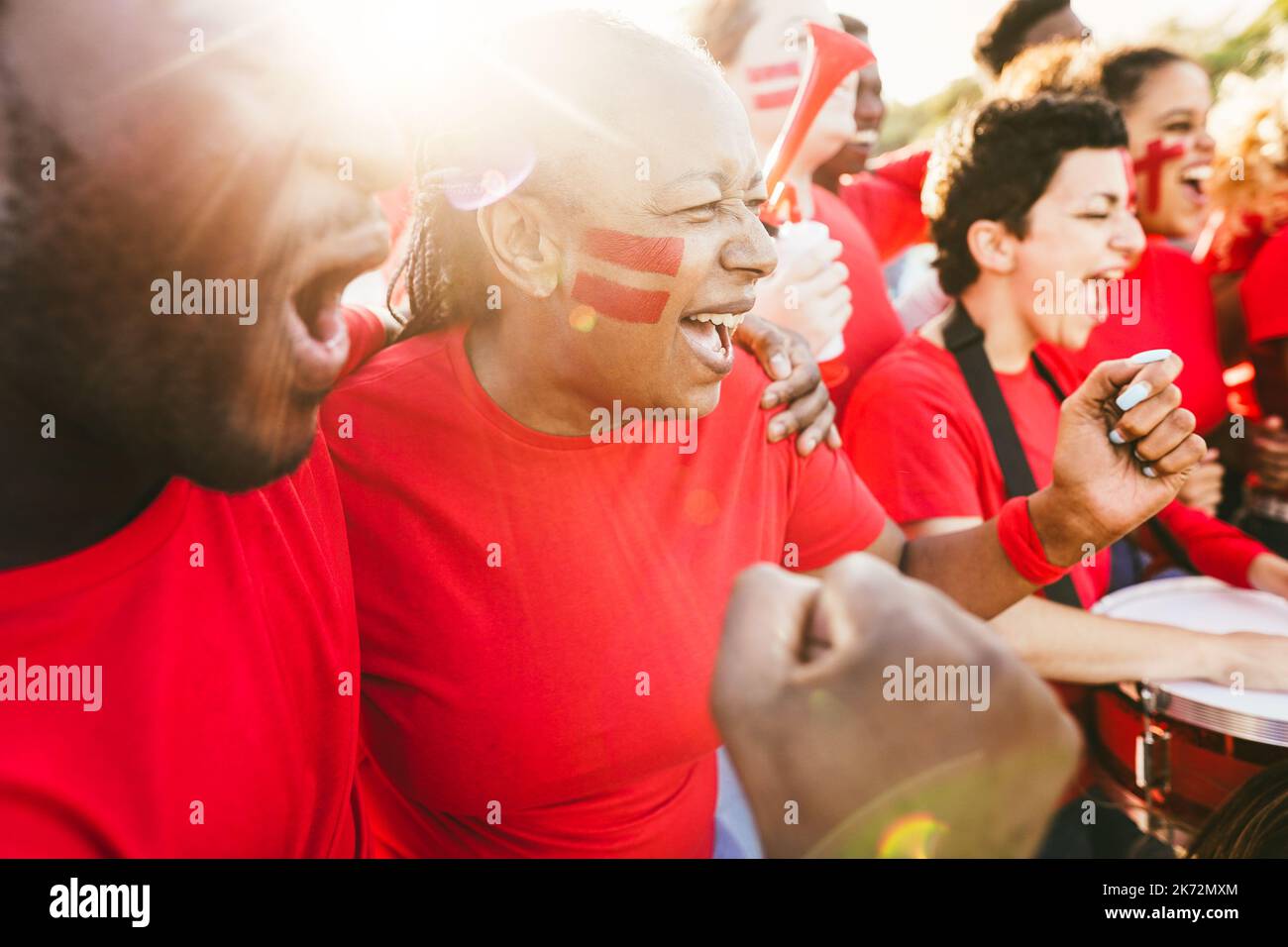 African red sport fans screaming while supporting their team - Football supporters having fun at competition event - Focus on senior woman face Stock Photo