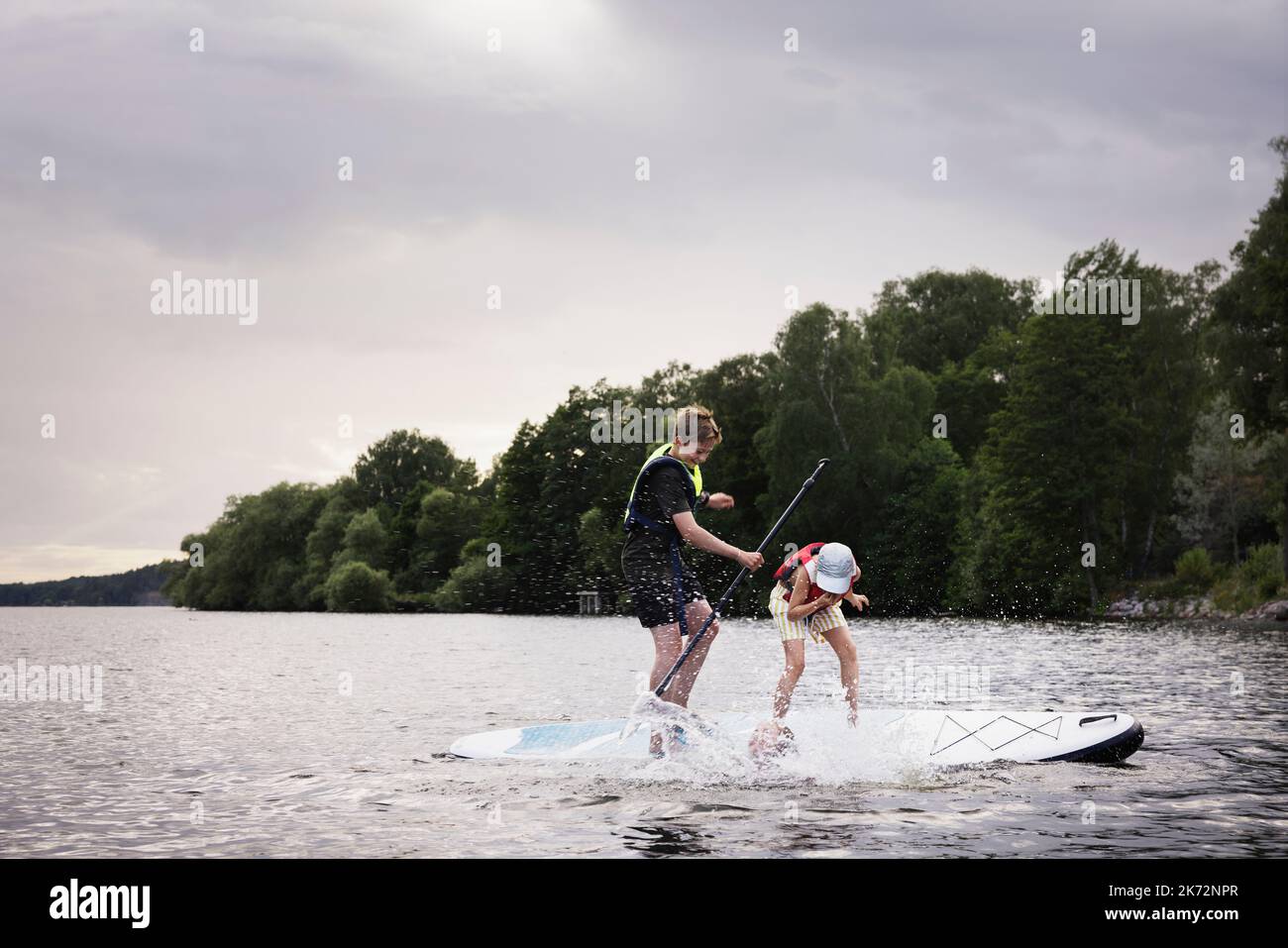 Siblings falling from paddle board on lake Stock Photo Alamy