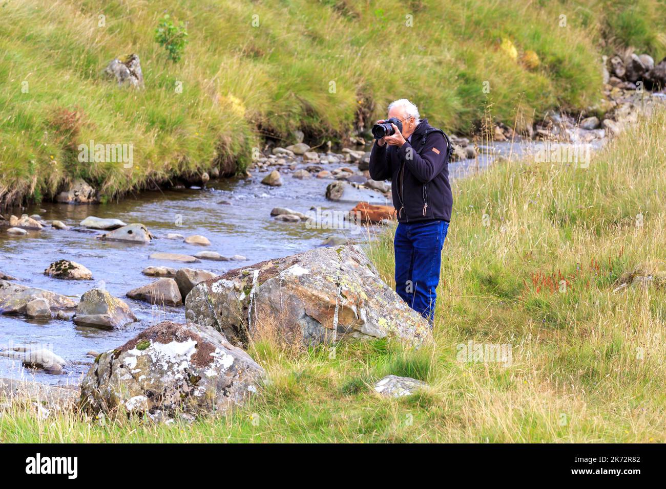 Photographer standing by a large rock with camera taking picture Stock Photo