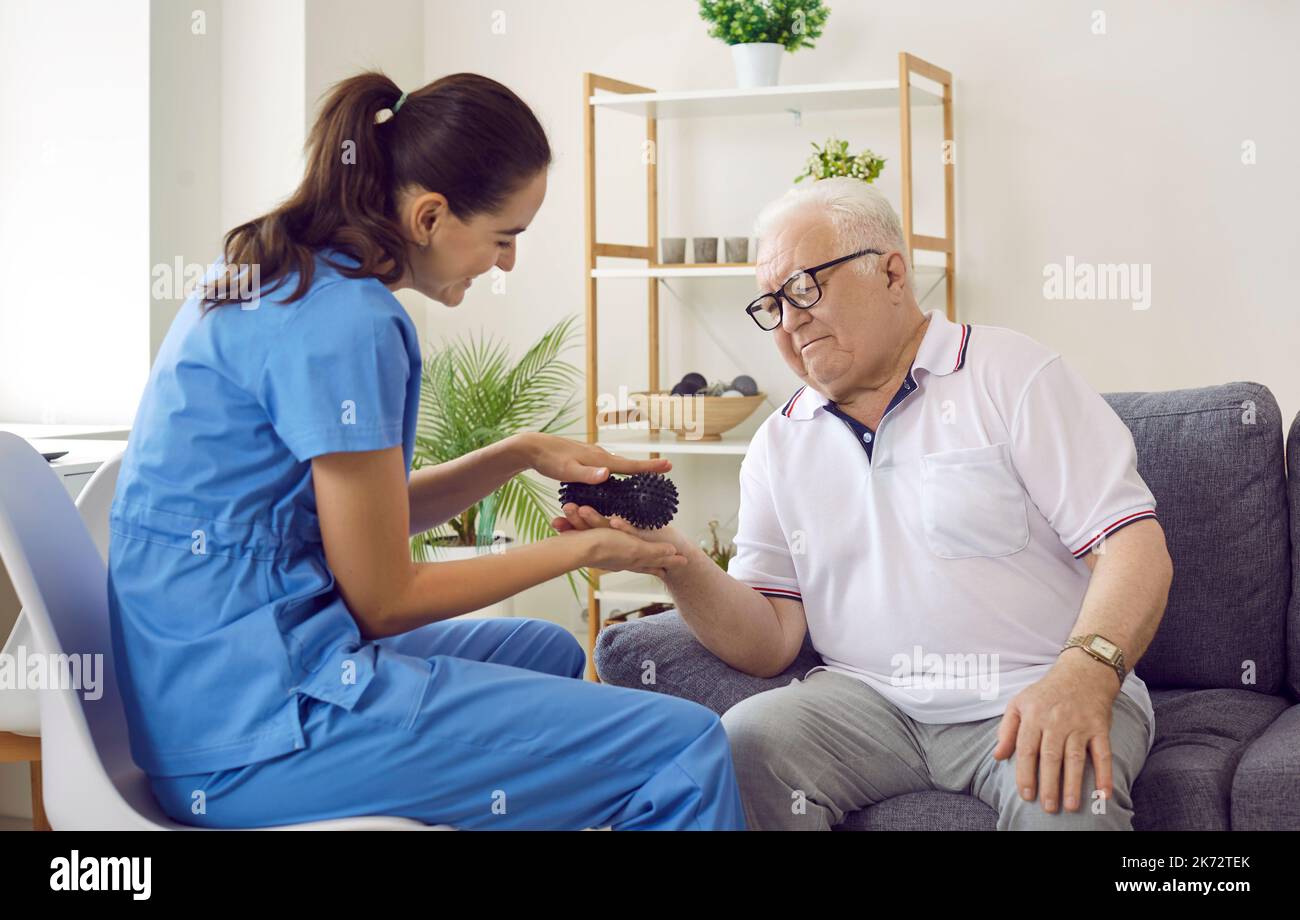 Friendly nurse or physiatrist holding rubber ball and doing hand massage to senior man Stock Photo