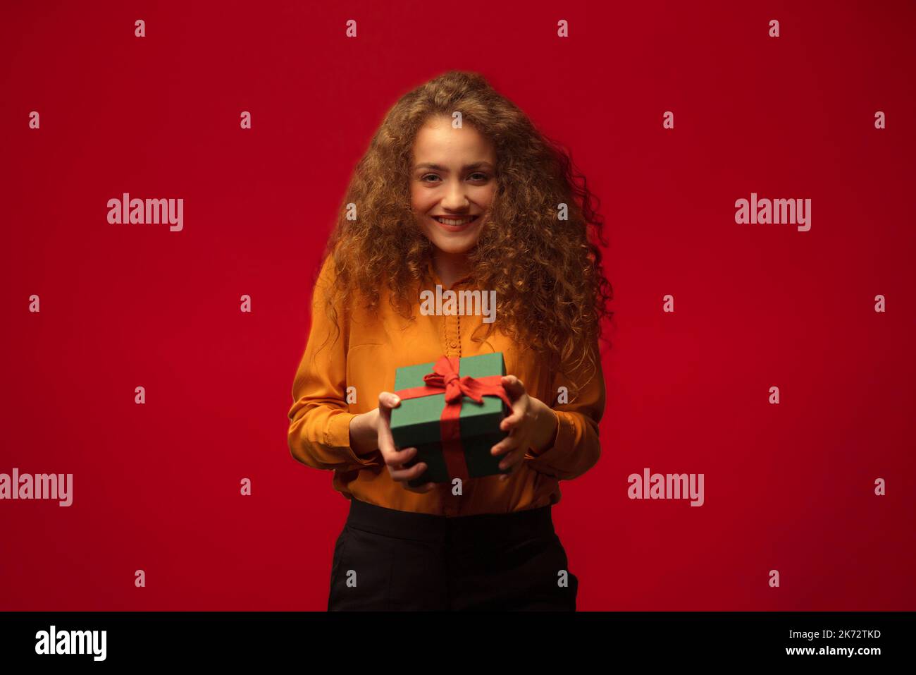 Portrait of happy young woman holding gift box, red background. Stock Photo