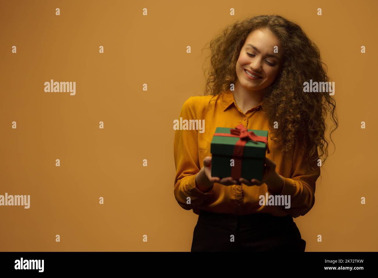 Portrait of happy young woman holding gift box, orange background. Stock Photo