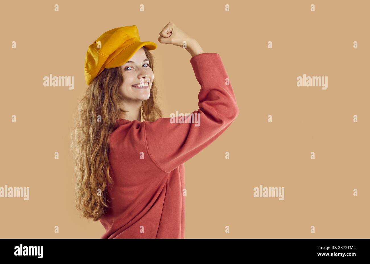Cheerful pretty young woman in autumn beret hat flexing her strong arm and smiling Stock Photo