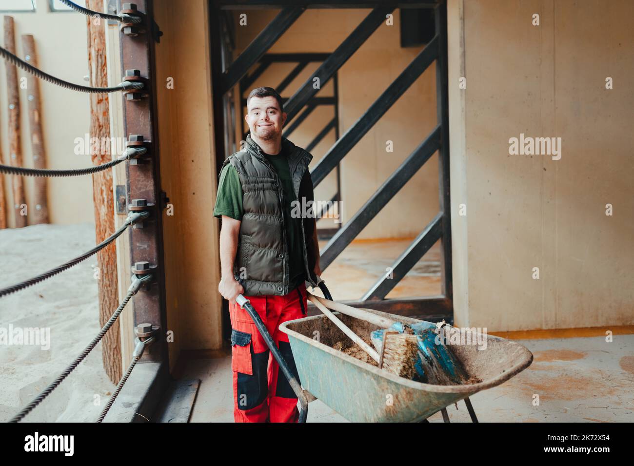 Caretaker with down syndrome in zoo pushing wheelbarrow after tidying