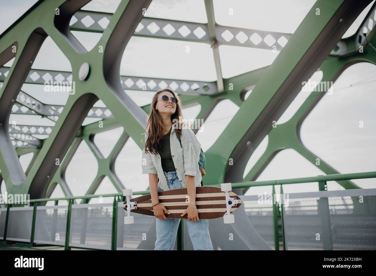 Young woman walking on city bridge with skateboard. Youth culture and commuting concept. Stock Photo