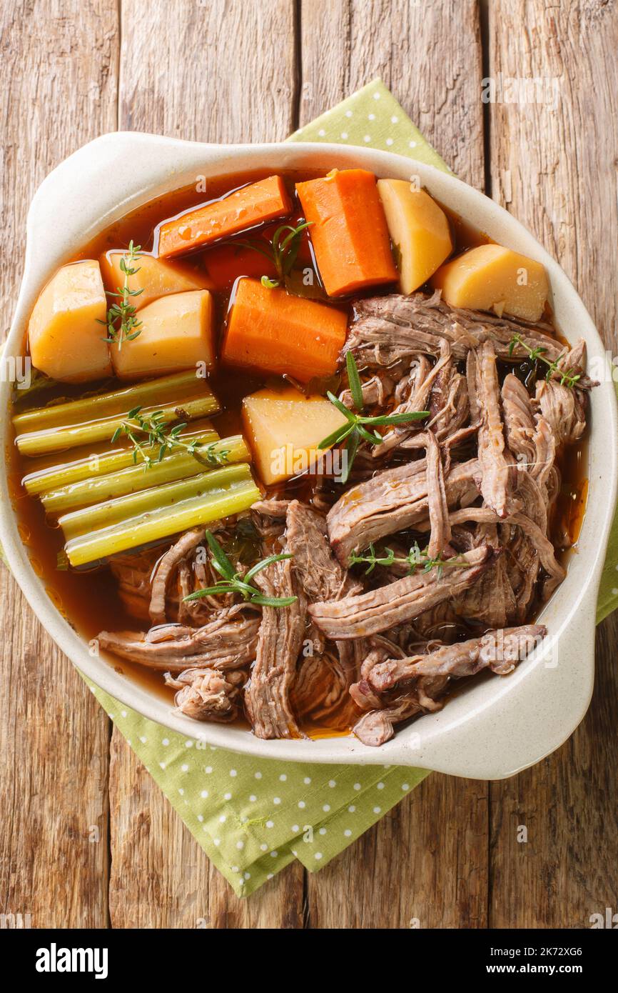 Homemade Slow Cooker Pot Roast with Carrots, Celery and Potatoes closeup in the bowl on the wooden table. Vertical top view from above Stock Photo