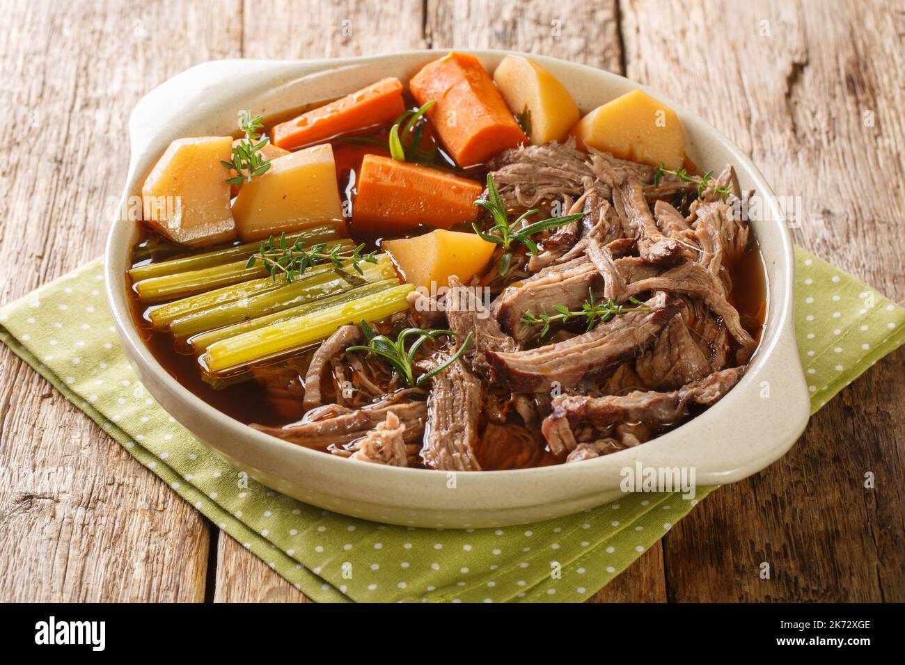 Slow cooked pot roast with carrots, celery, potatoes, garlic and gravy closeup in the bowl on the wooden table. Horizontal Stock Photo