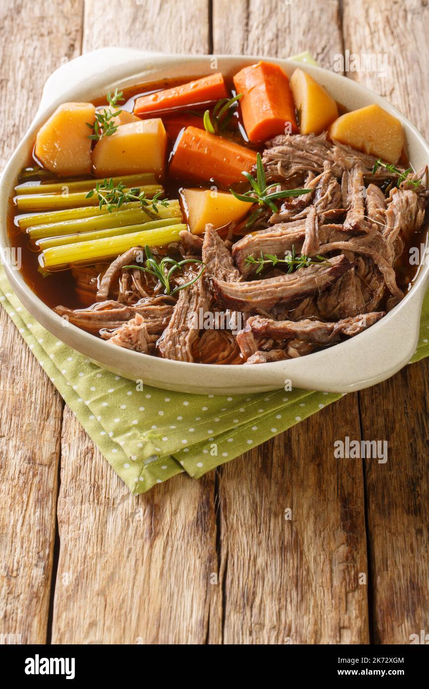 delicious beef pot roast with potatoes, celery and carrots with thyme and rosemary closeup in the bowl on the wooden table. Vertical Stock Photo