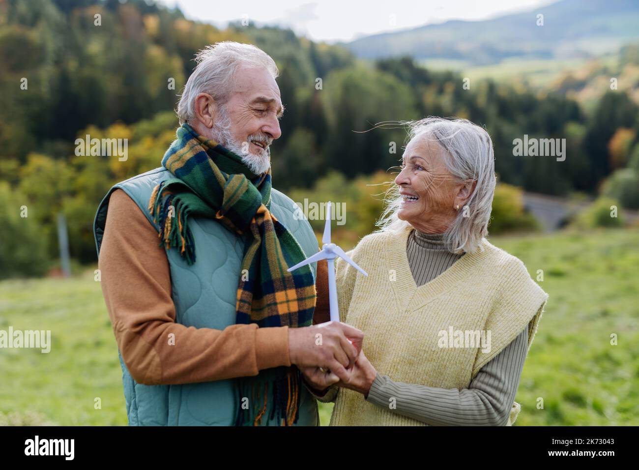 Senior couple holding plastic model of wind turbine in nature, concept of future, ecology and renewable resources, message for next generation Stock Photo