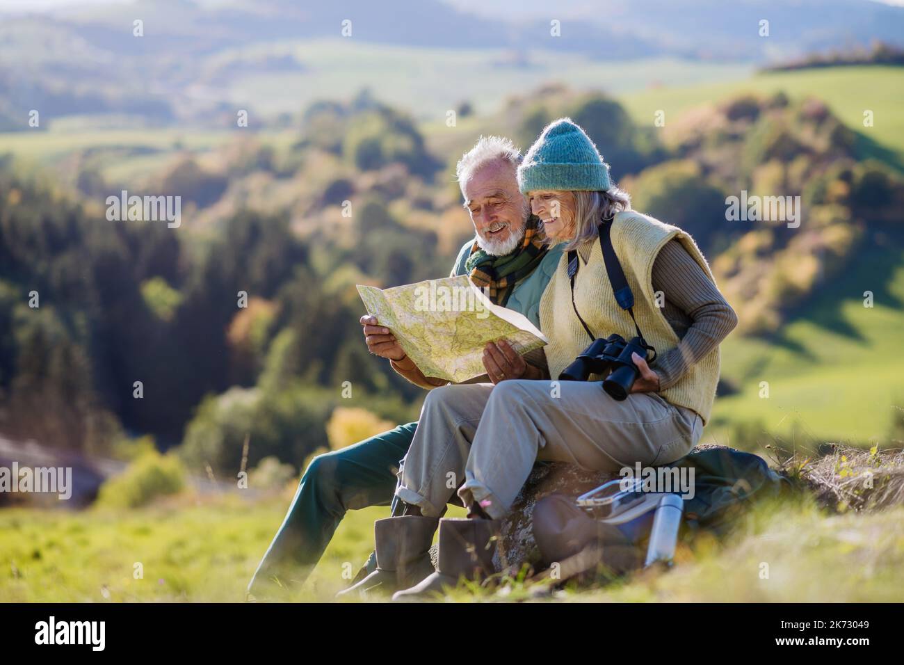 Senior couple having break, looking into paper map during hiking in autumn nature. Stock Photo