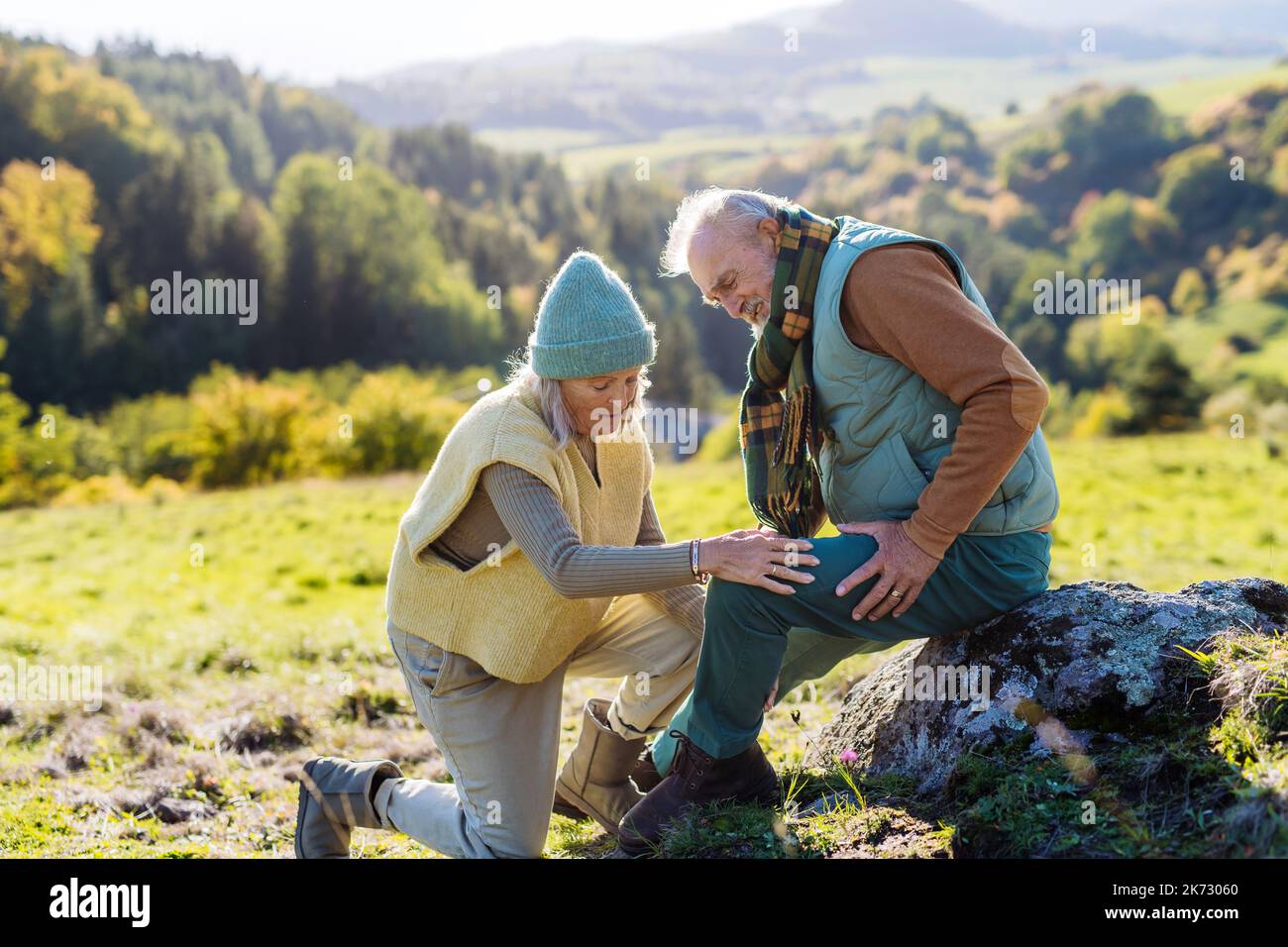 Senior man with hurting knee resting during autumn walk, his wife taking care of him. Stock Photo