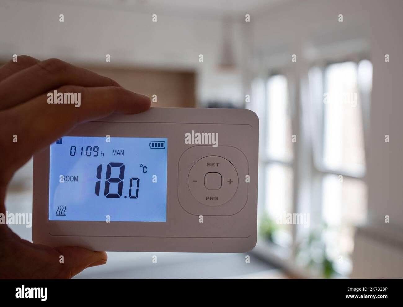 Close up of thermostat heating control panel with heater in background in cold room because of gas restriction and energy crisis Stock Photo