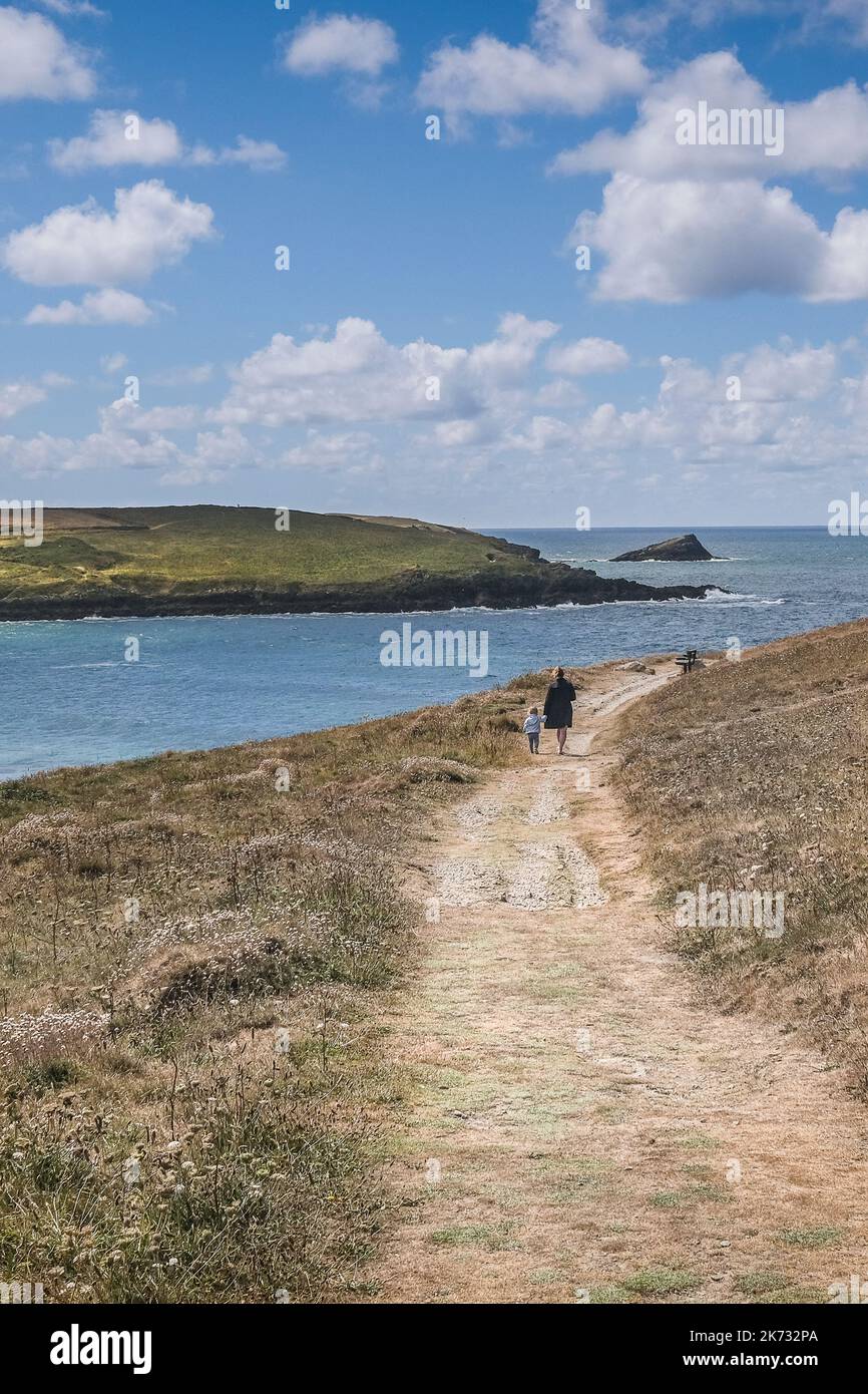 A mother and toddler walking holding hands along a rough footpath on Pentire Point East on the coast at Newquay in Cornwall in the UK. Stock Photo