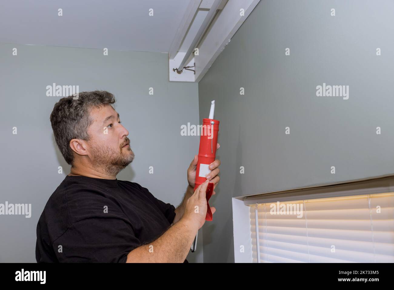 Construction worker uses syringe to fill seam between cornice and wall