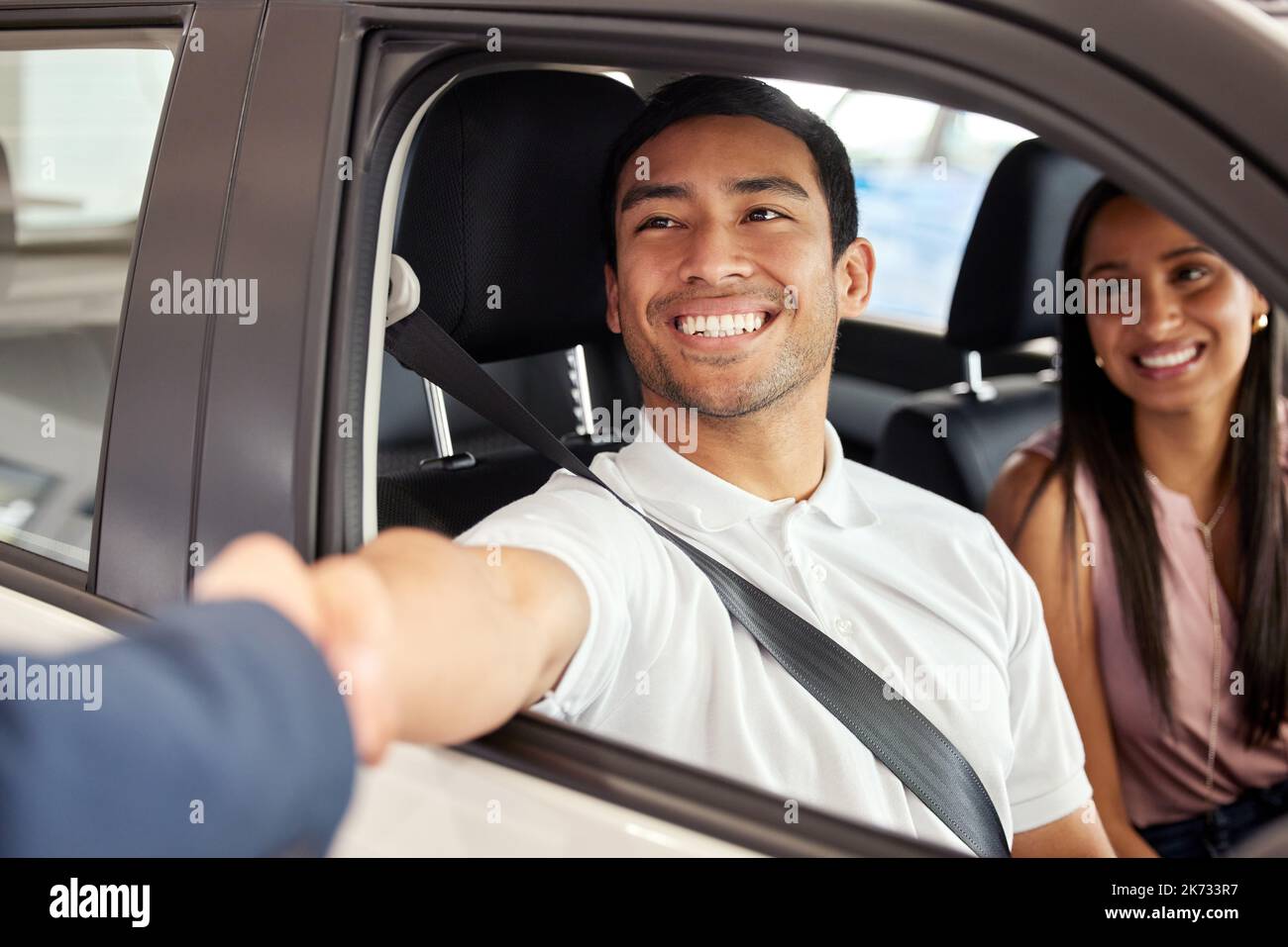 I wish you many happy miles in your new car. a young couple leaving a car dealership with their new car. Stock Photo